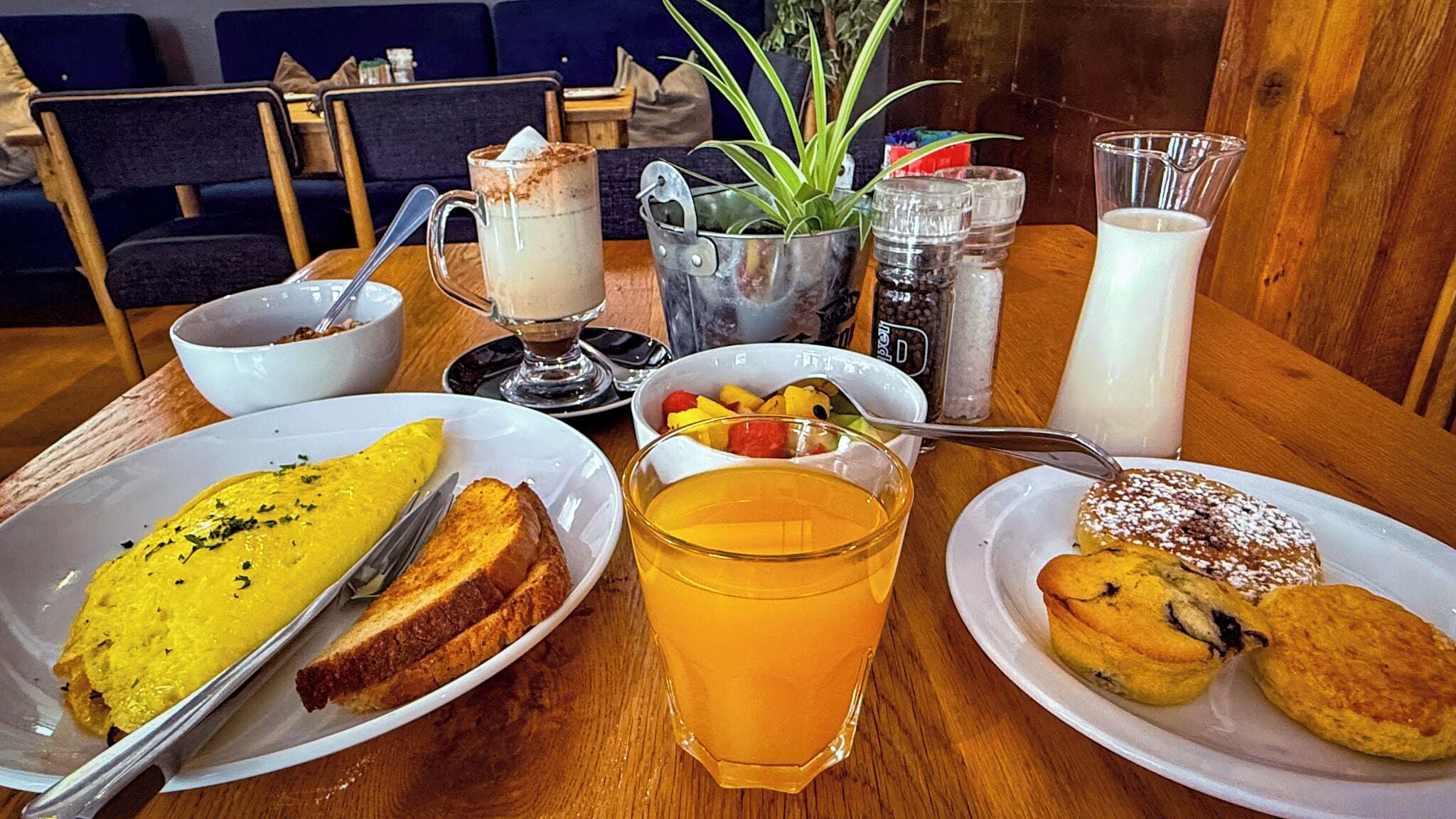 A breakfast table with plates of food, a glass of orange juice, and a pitcher of milk.