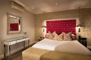 A bedroom with a large bed, a vanity with a mirror, and a red upholstered headboard.