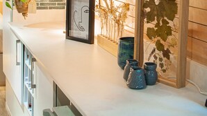 Un plafond en bois, un comptoir blanc orné d’œuvres d’art encadrées et un pot de fleurs suspendu.