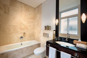 Une salle de bain équipée d’une baignoire, de toilettes et d’un lavabo, avec des murs en marbre et un grand miroir.