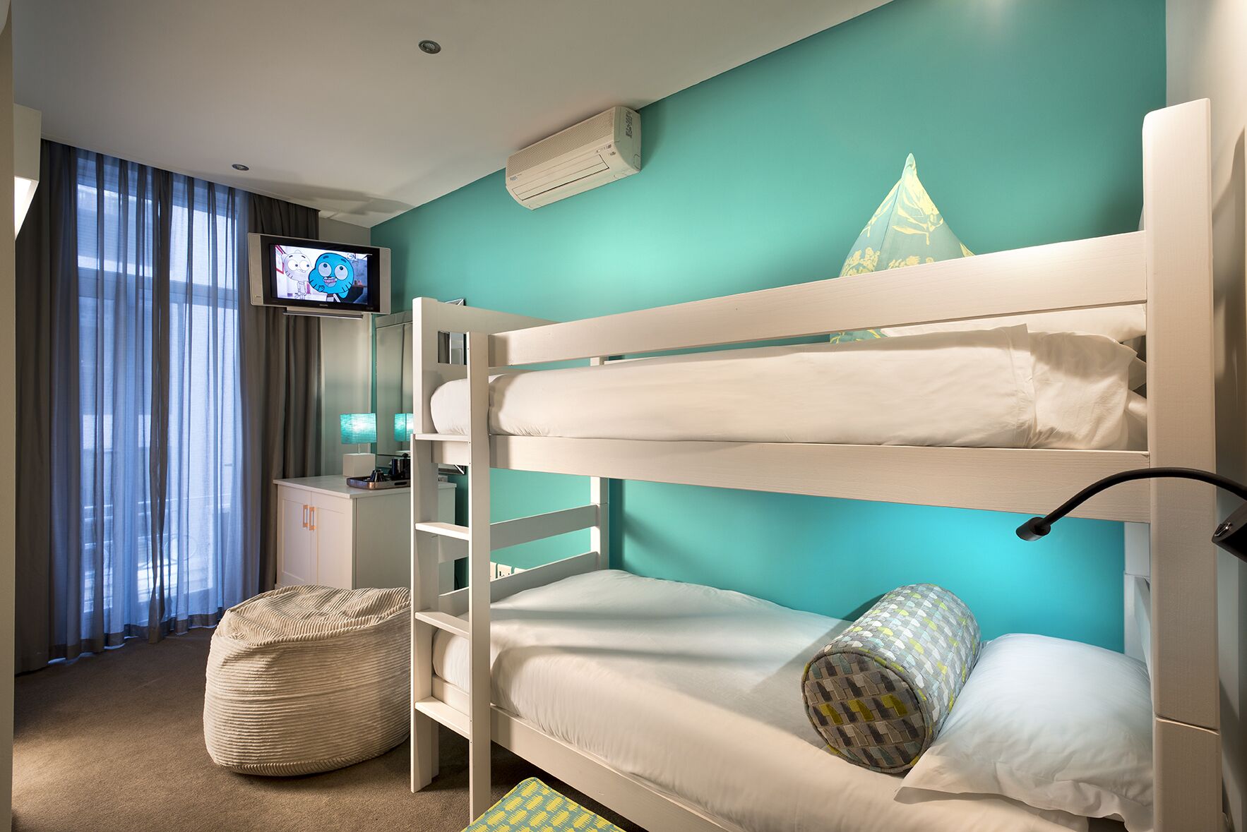 A bunk bed room with a television, a desk, and a window with curtains.