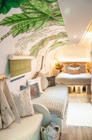 A cozy bedroom with a bed, pillows, a wall-mounted TV, and a ceiling mural.