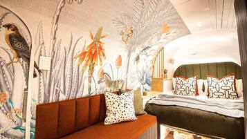 Ein modernes Schlafzimmer mit einer großen Wandmalerei, einer Couch und einem Bett mit gemusterten Kissen.