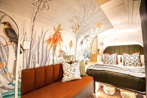 A modern bedroom with a large mural, a sofa, and a bed with patterned pillows.