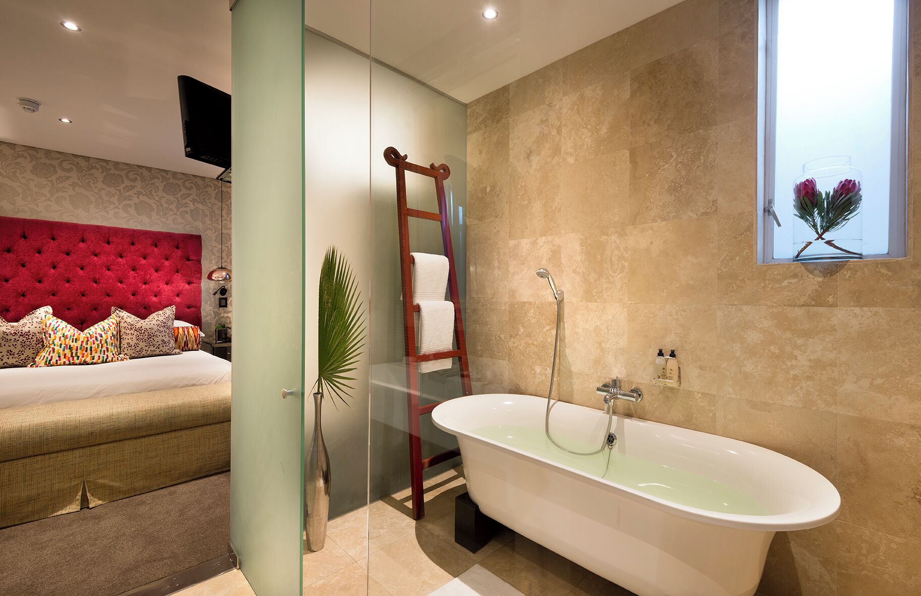 Un baño moderno con una bañera independiente, un separador de vidrio y un cabecero tapizado en rojo.