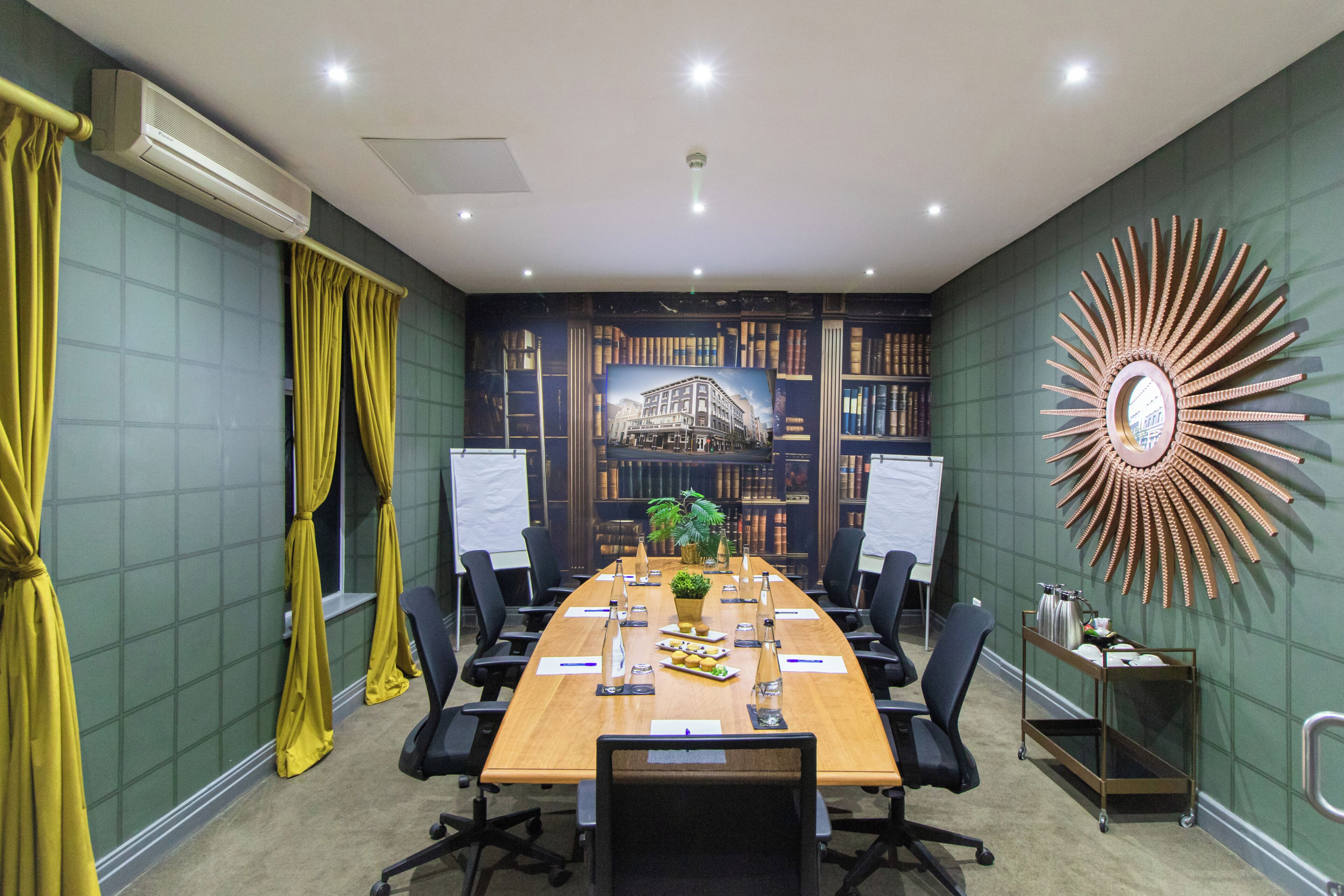 A conference room with a long table, chairs, a whiteboard, and a decorative sunburst wall piece.