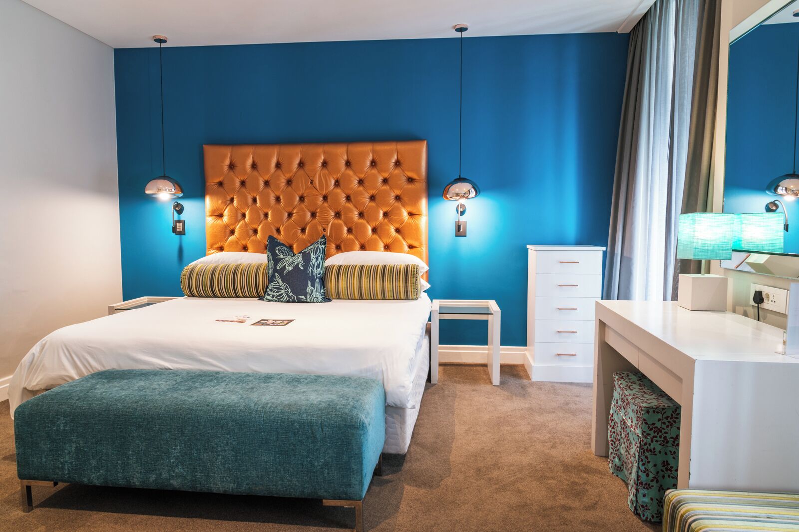 Una camera d'albergo moderna con una testiera trapuntata, un letto grande, un comodino, una scrivania e uno specchio.