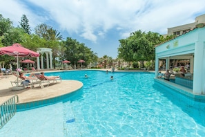 A swimming pool with lounge chairs and umbrellas, surrounded by trees and a building with a sign. - Crown Resorts Henipa (Oroklini)