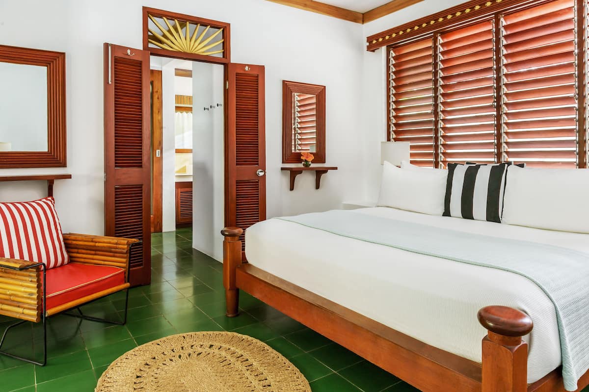 A bedroom with a wooden bed, a red and white striped chair, and a green tiled floor.