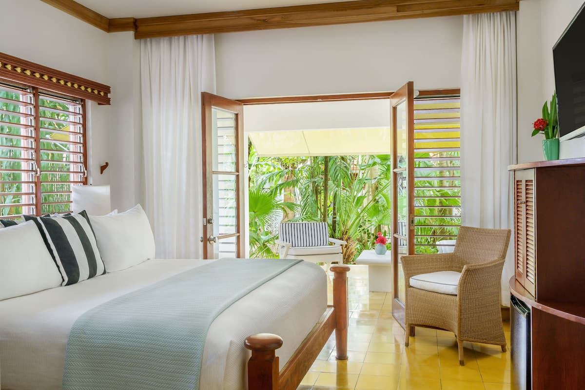 A bedroom with a bed, a chair, and a view of greenery outside.