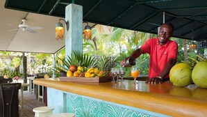 Zona de bar con temática tropical, con barra de madera, varias frutas y una pared decorativa.