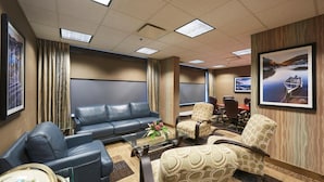 A conference room with a blue sofa, patterned chairs, a glass coffee table, and framed pictures on the walls. - Capital Hotel (St. John's)