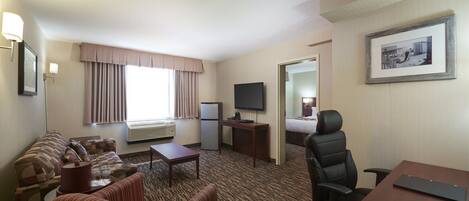 A hotel room with a sofa, armchairs, a desk, a television, and a bed.