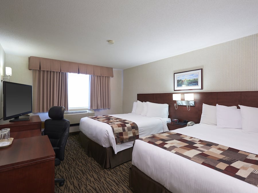 A hotel room with two beds, a desk with a TV, and a window with curtains.