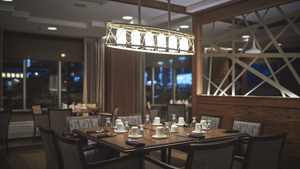 A dining area with a rectangular table set for six, surrounded by chairs. A modern pendant light hangs above the table. - Capital Hotel (St. John's)