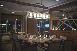 A dining area with a rectangular table set for six, surrounded by chairs. A modern pendant light hangs above the table. - Capital Hotel (St. John's)