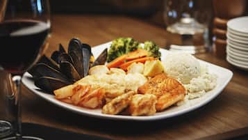 Un plato de mariscos y verduras con una copa de vino tinto sobre una mesa de madera.