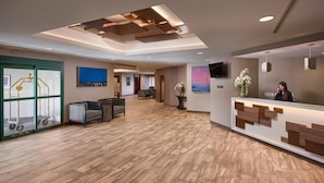 A modern hotel lobby with a wooden floor, a reception desk, a large painting, and a television on the wall. - Capital Hotel (St. John's)