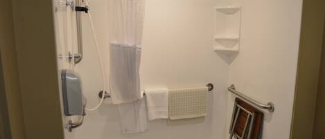 Ducha a pie con cabezal de ducha de mano, cerramiento de vidrio, toalla blanca y barra de apoyo.