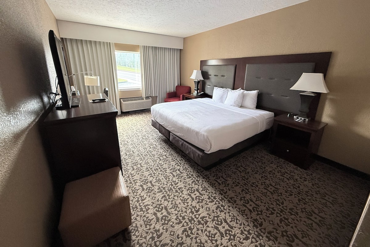 A hotel room with a large bed, a desk, a chair, a nightstand, and a window with curtains.
