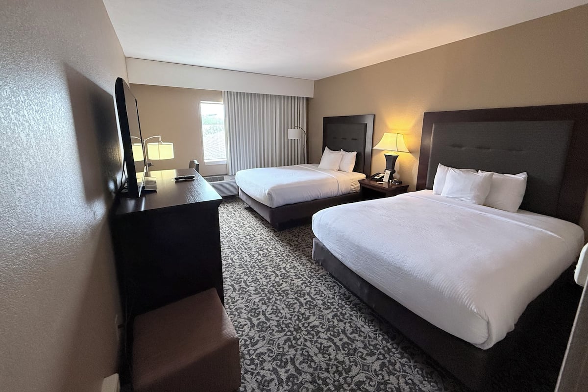 A hotel room with two beds, a desk, a chair, a lamp, and a large mirror.