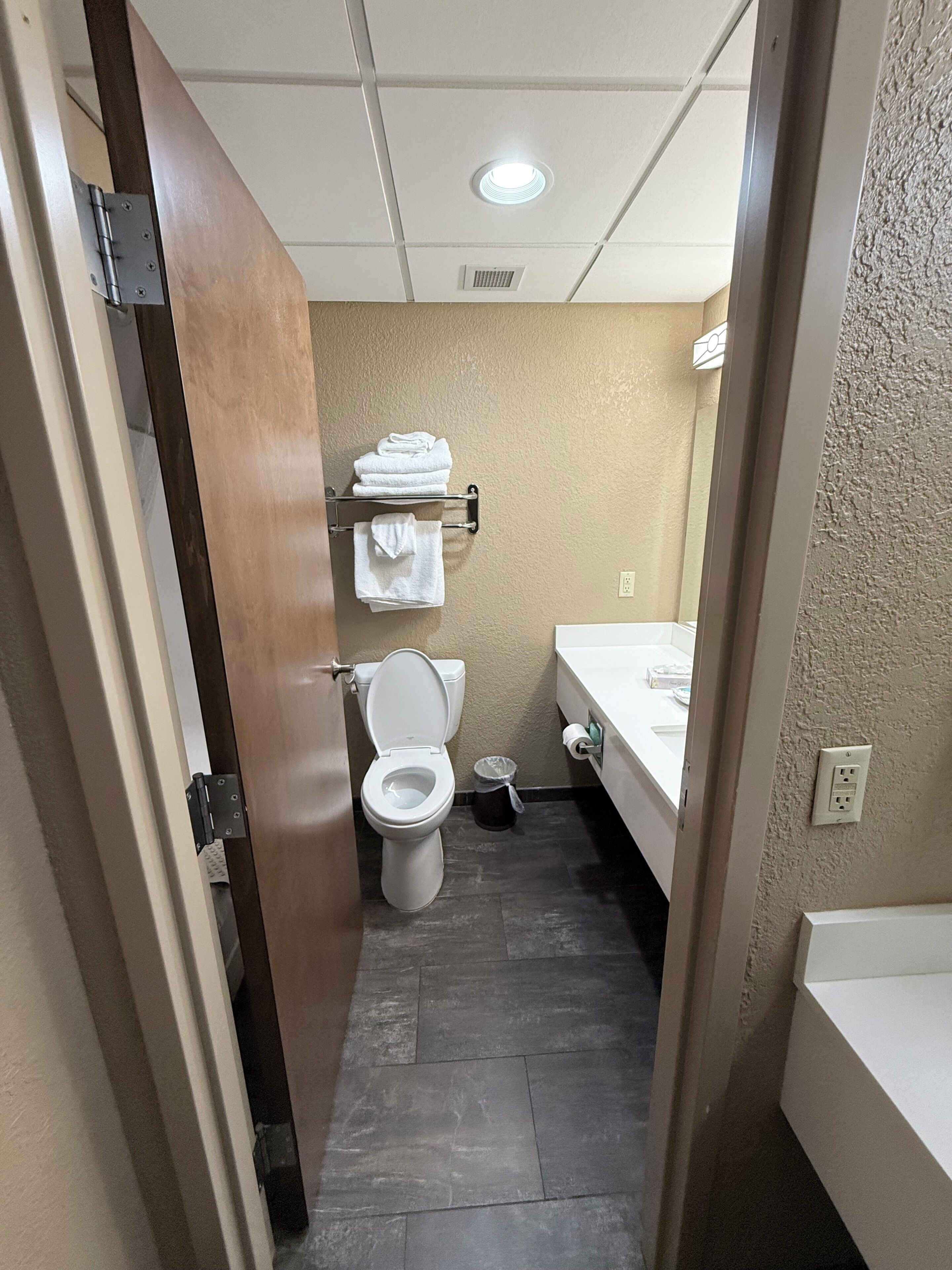 A compact bathroom with a toilet, a towel rack, a trash bin, and a sink.