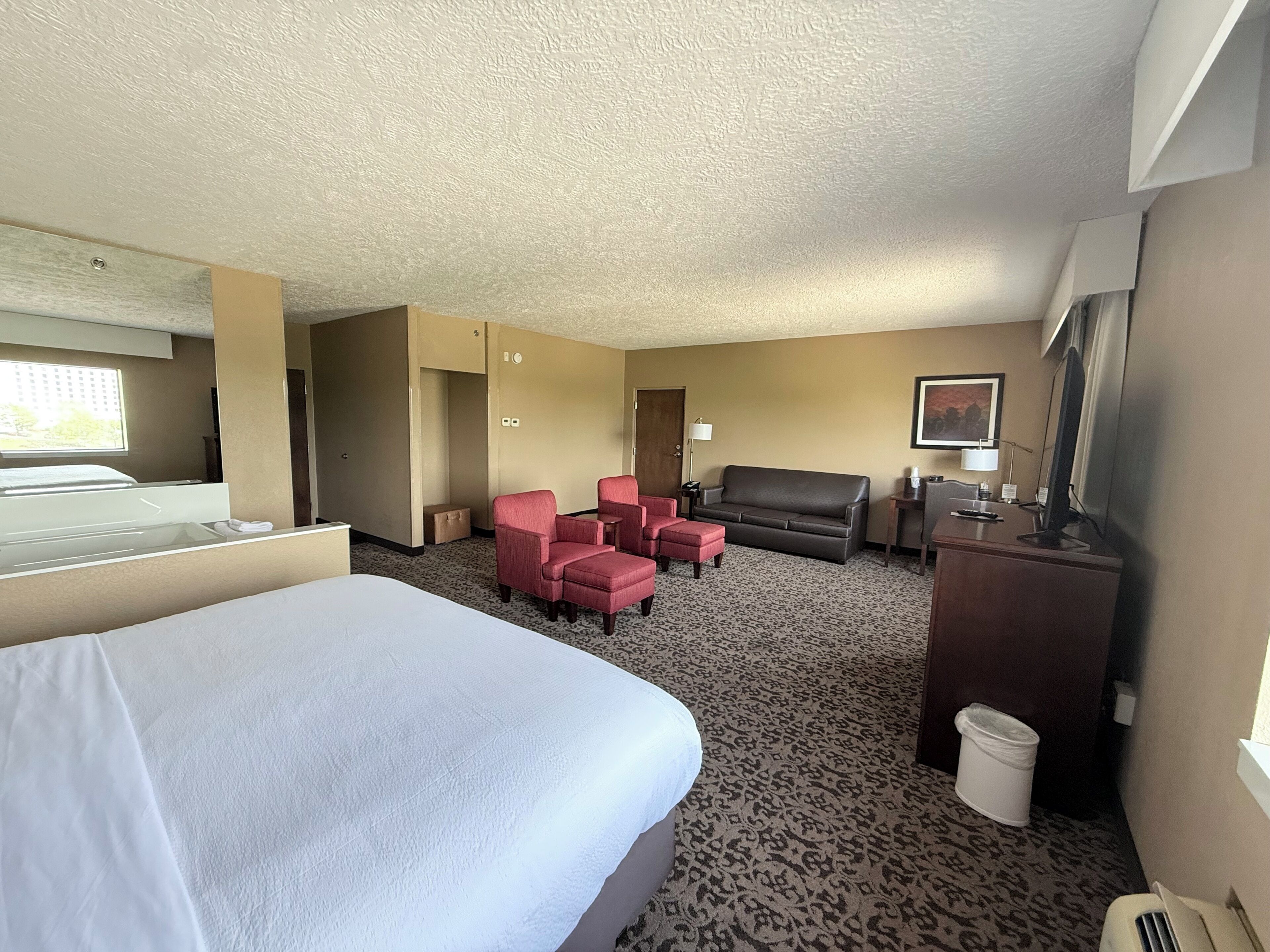 A hotel room with a bed, a desk with a computer, a sofa, and two armchairs.