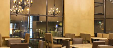 Un restaurante con varias mesas y sillas, ventanas amplias y candelabros.