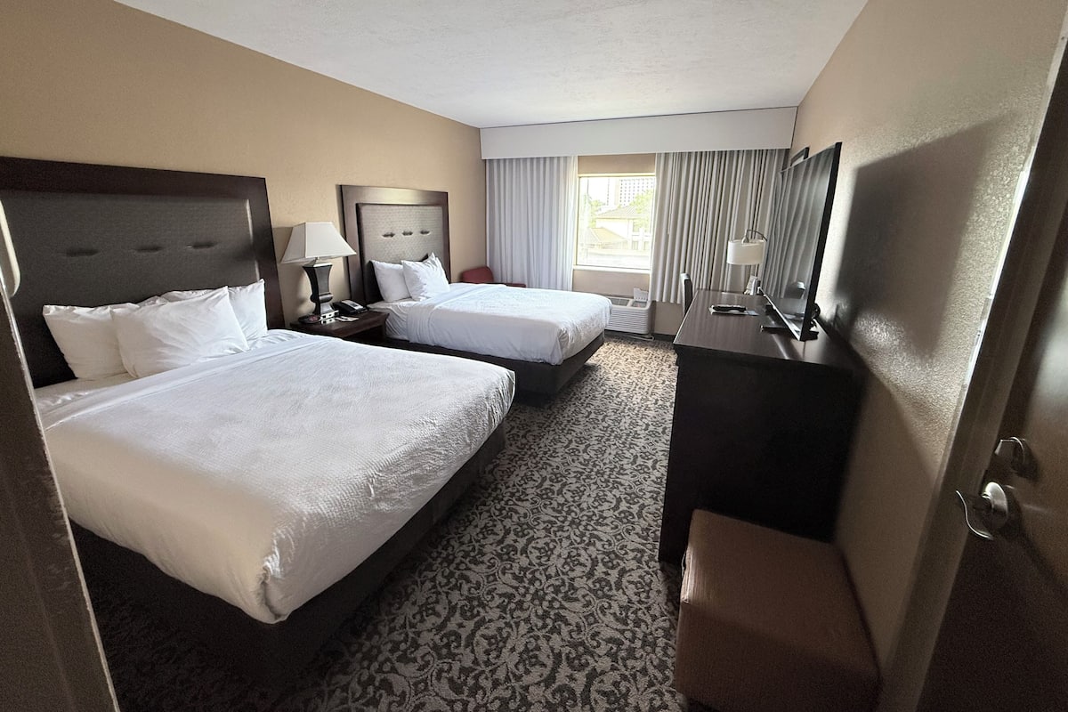 A hotel room with two beds, a desk, a chair, a lamp, a telephone, and a window with curtains.