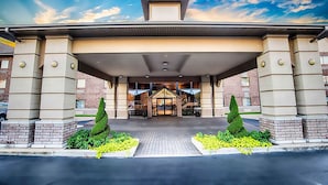 A hotel entrance with a covered walkway, brick facade, and symmetrical landscaping. - Grand Oaks Hotel (Branson)