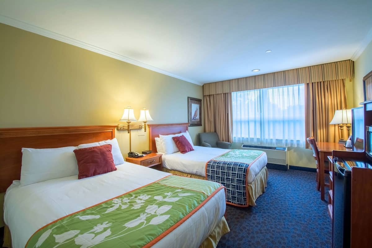A hotel room with two beds, a desk, a chair, a TV, and a window with curtains.
