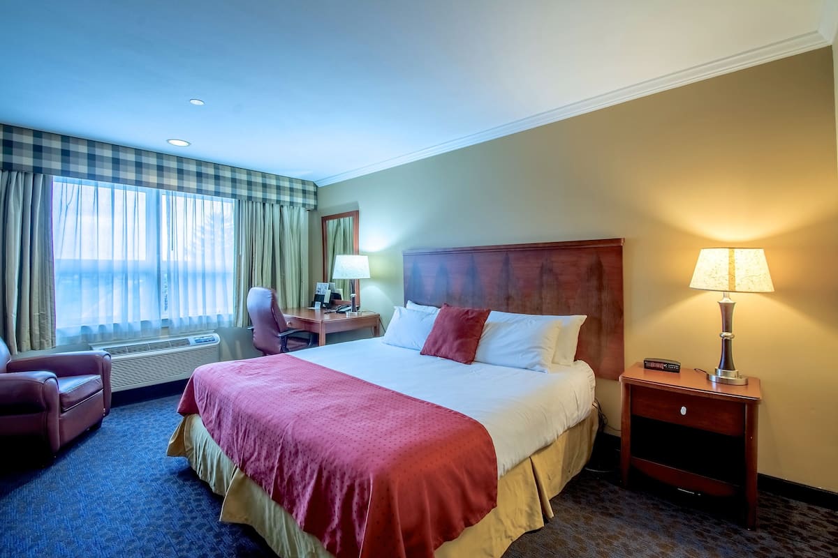 A hotel room with a large bed, a desk, a chair, a lamp, and a window with curtains.