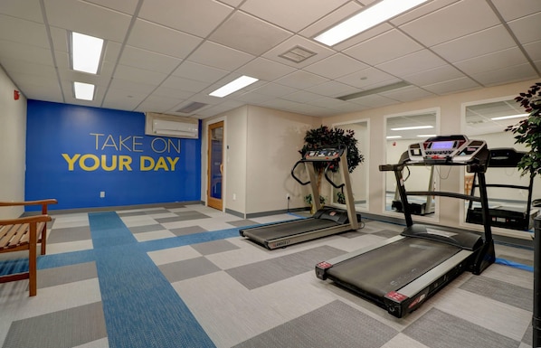 Une salle de sport équipée de tapis de course, d’un mur bleu décoré de messages motivants et d’un sol à carreaux.
