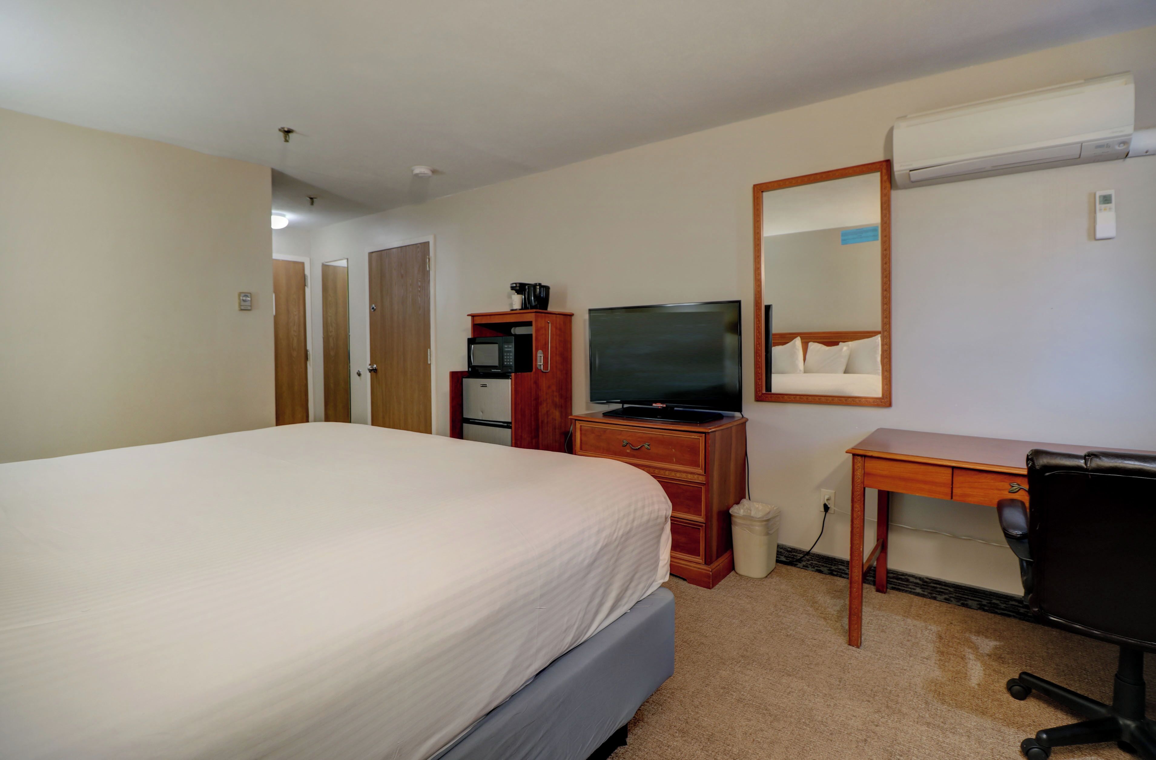 Une chambre d’hôtel avec un grand lit, un bureau avec un ordinateur, une télévision, un four à micro-ondes et une poubelle.