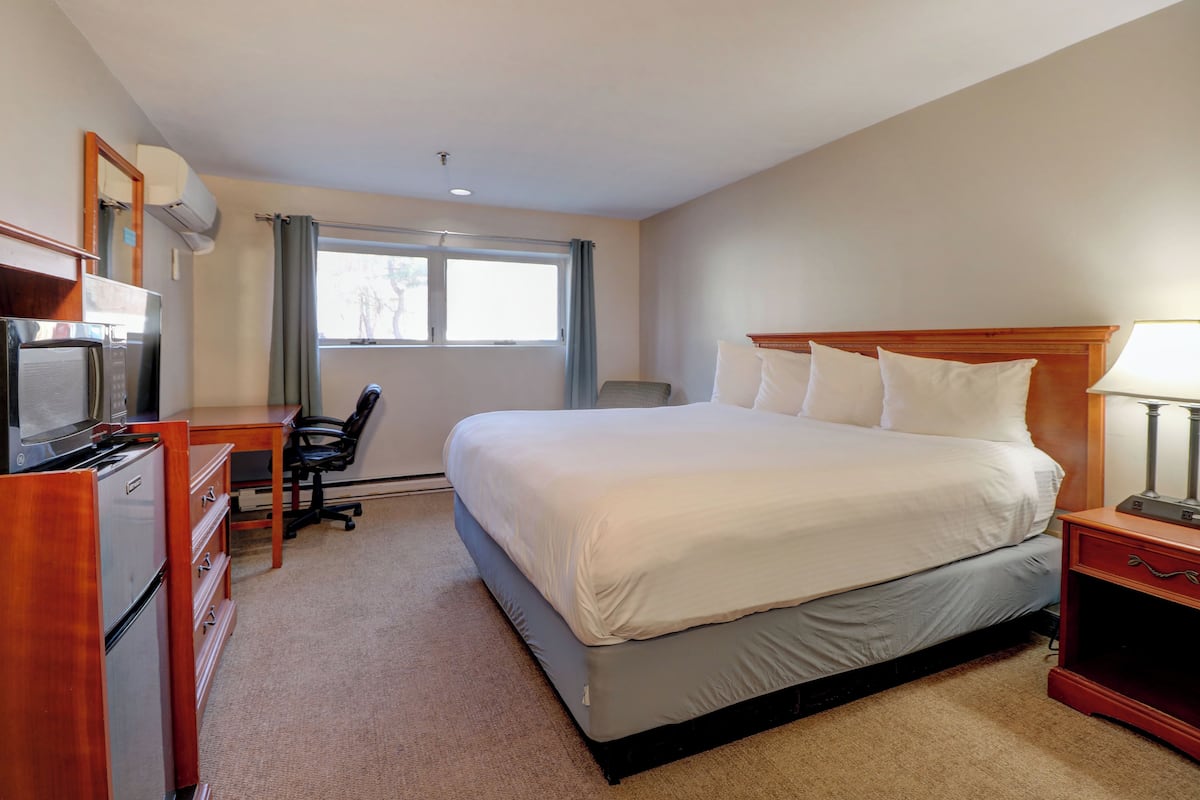 A hotel room with a bed, desk, chair, and a TV.