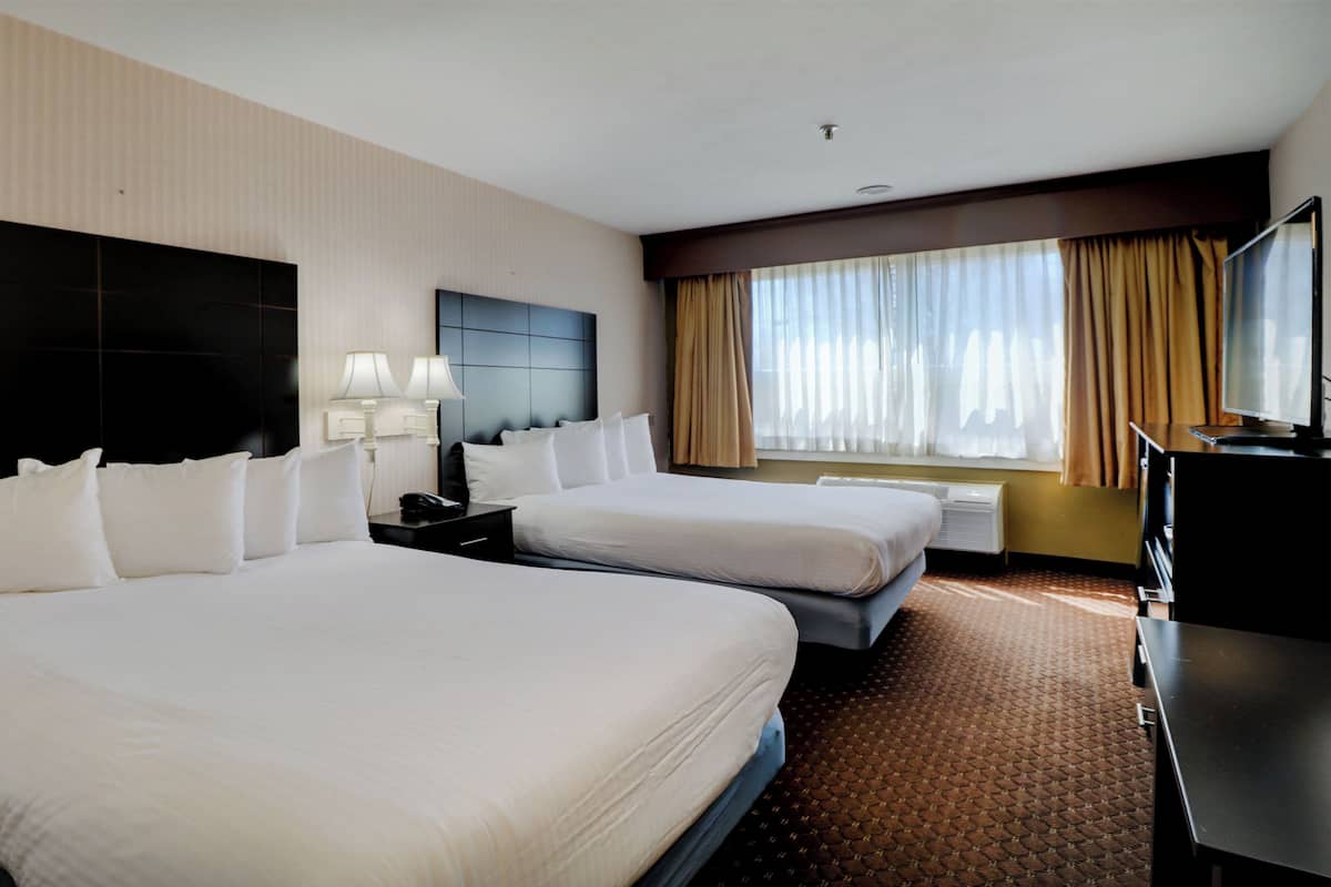 A hotel room with two beds, a TV, a desk, and a window with curtains.