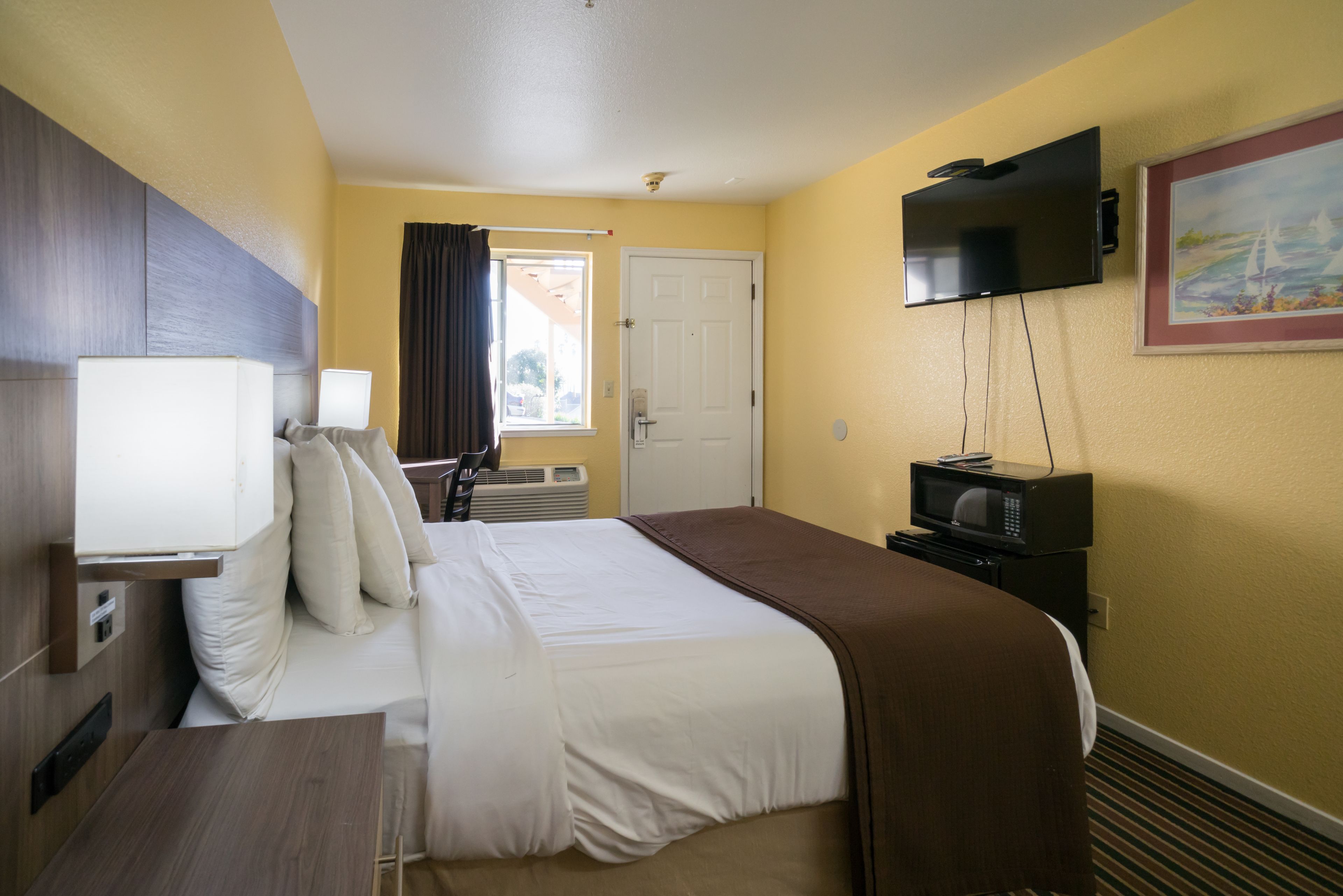 A hotel room with a bed, bedside table, TV, and a painting on the wall.