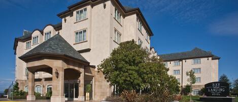 A large, multi-story hotel with a prominent entrance, a landscaped garden, and a clear blue sky.