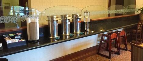 A hotel reception area with a counter, coffee machines, and seating.