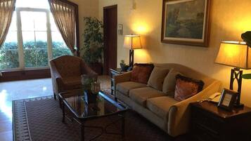 Una sala de estar con sofá, sillón y mesa de centro, un cuadro en la pared y una ventana con cortinas.