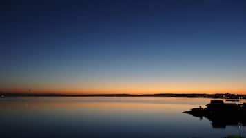 A calm lake at dusk with a clear sky, a distant shoreline, and a small jet visible.