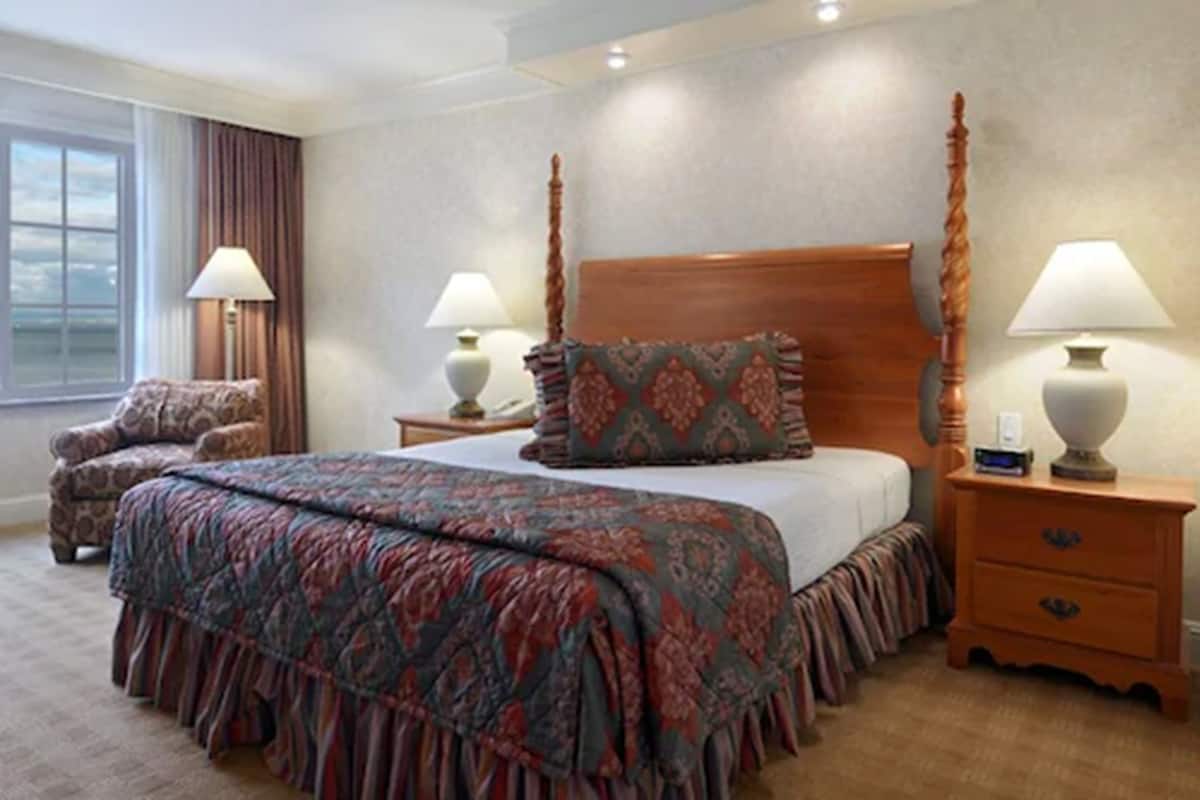 Een hotelkamer met een groot bed, twee nachtkastjes met lampen, een stoel en een raam met gordijnen.
