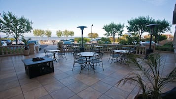 An outdoor patio with multiple tables and chairs, a black crate, and potted plants.