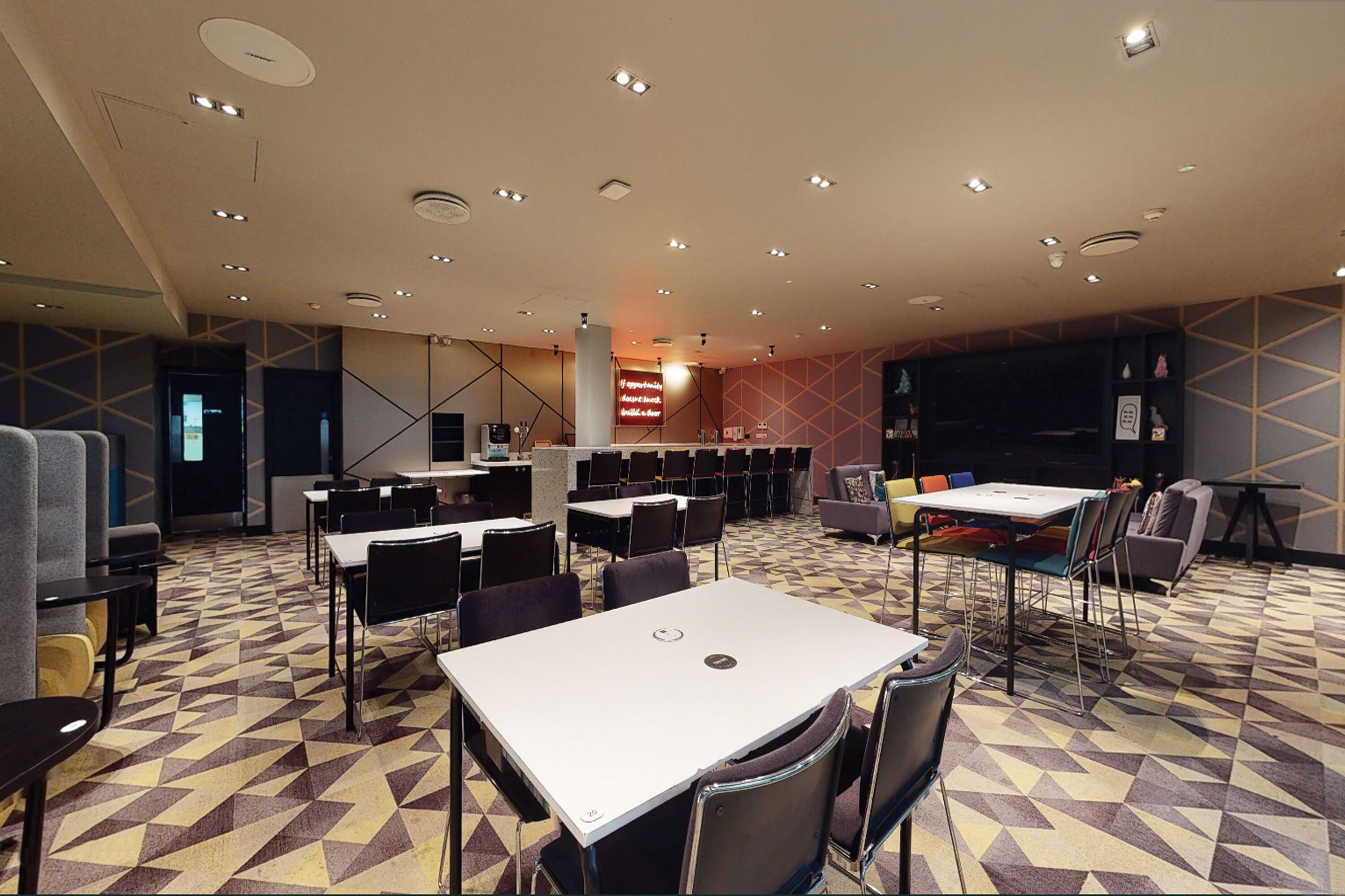 Un salón de conferencias con varias mesas y sillas, un escenario con atril, y un piso con estampado.