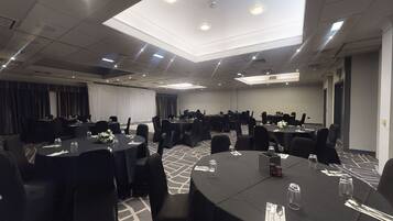 Un salón de conferencias con mesas redondas, sillas negras y un área de escenario con cortinas.