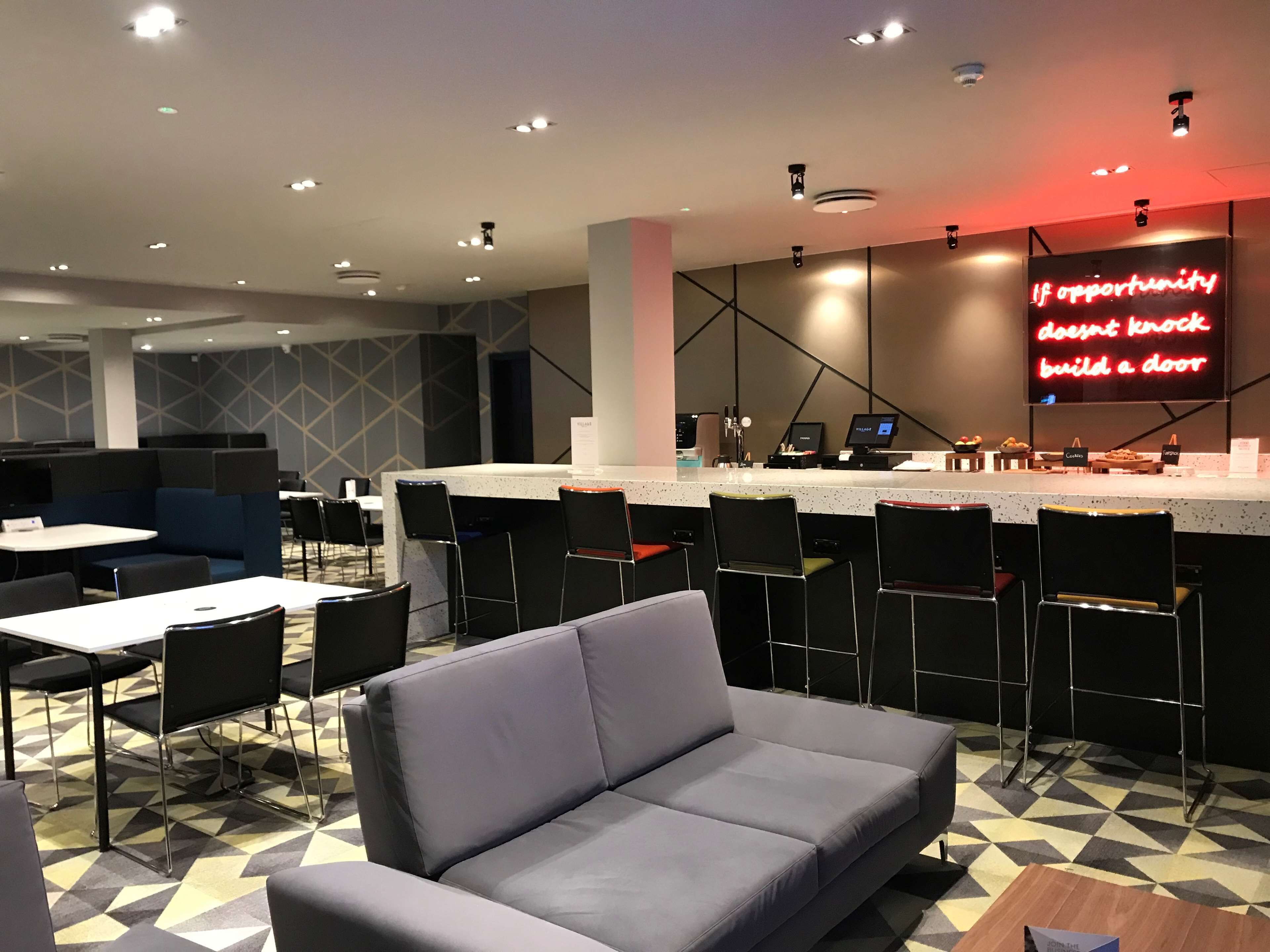 A modern restaurant with a bar area, seating arrangements, and a neon sign on the wall.