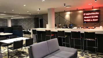 Un restaurante moderno con área de bar, disposición de mesas y un letrero de neón en la pared.