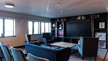A modern lounge area with seating, a large flat-screen TV, and a bookshelf.