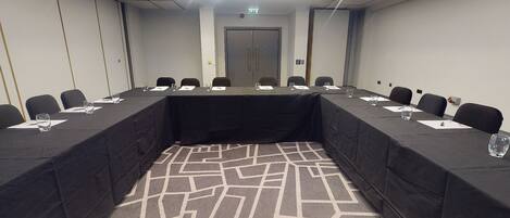 A conference room with a long table, chairs, and a patterned carpet.