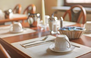 A dining table set with a white cup and saucer, a basket of bread, and a salt and pepper shaker. - Entrée Hotel Glinde (Glinde)